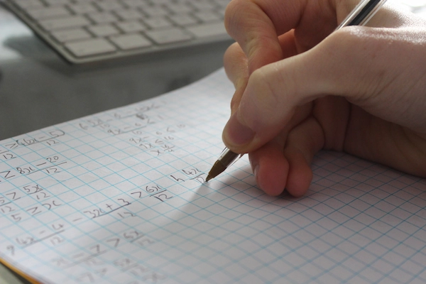 a close up of someone writing out a math formula on graph paper