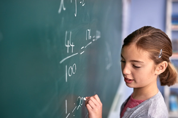 young female student writing fractions on a chalkboard