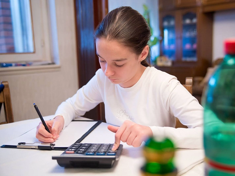 girl at a table learning algebra and using a calculator to solve a problem